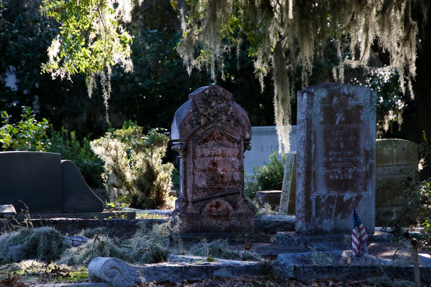 An American flag rests against an old inscribed stone gravestone.