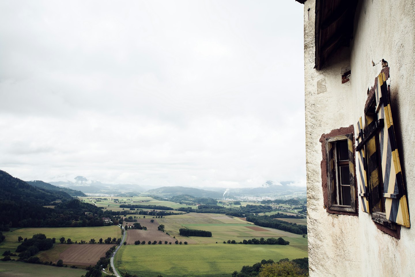 Rolling green and brown fields and forests with a winding road.