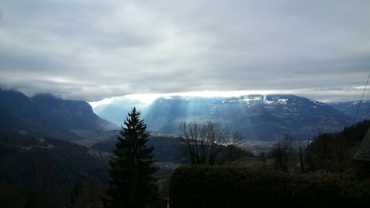 Sunlight breaks through clouds over snow-capped mountain peaks.